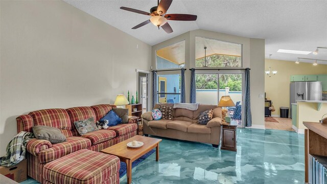 living room with a textured ceiling, ceiling fan with notable chandelier, and vaulted ceiling with skylight