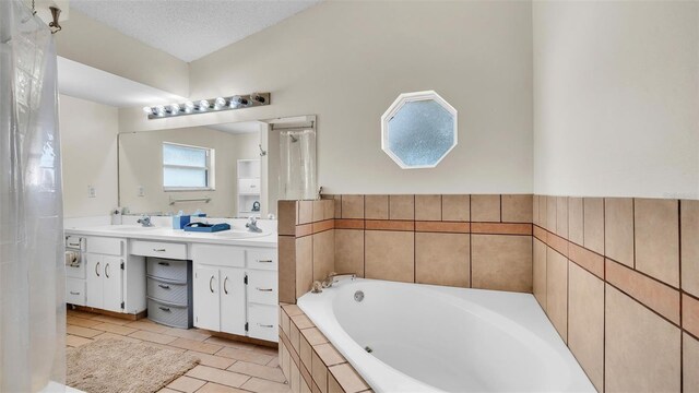 bathroom with a textured ceiling, tile patterned floors, vanity, and tiled tub