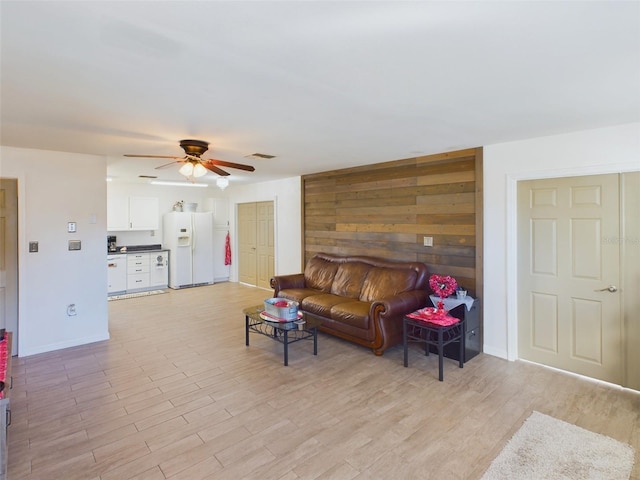 living room with wooden walls, ceiling fan, and light wood-type flooring