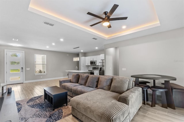 living room with sink, ceiling fan, and a tray ceiling