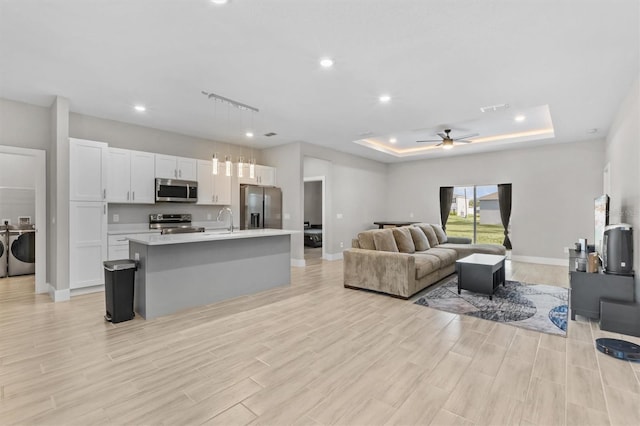 living room featuring sink, washer and dryer, light hardwood / wood-style flooring, a raised ceiling, and ceiling fan