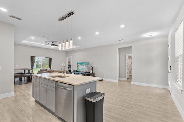 kitchen featuring sink, hanging light fixtures, light wood-type flooring, dishwasher, and a kitchen island with sink