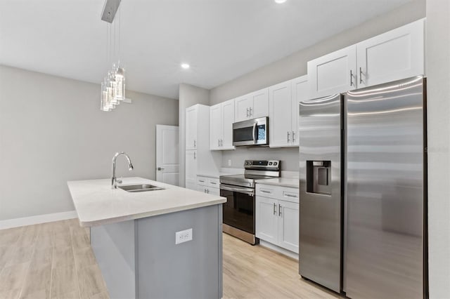 kitchen featuring sink, decorative light fixtures, appliances with stainless steel finishes, a kitchen island with sink, and white cabinets