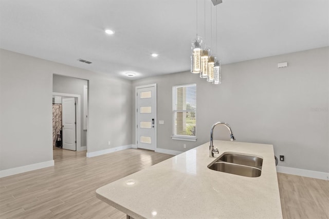 kitchen featuring hanging light fixtures, light wood-type flooring, sink, and a center island with sink