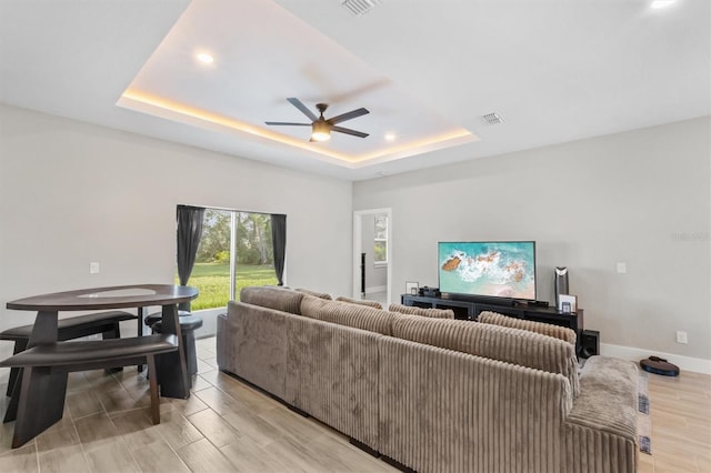 living room with ceiling fan, a tray ceiling, and light wood-type flooring