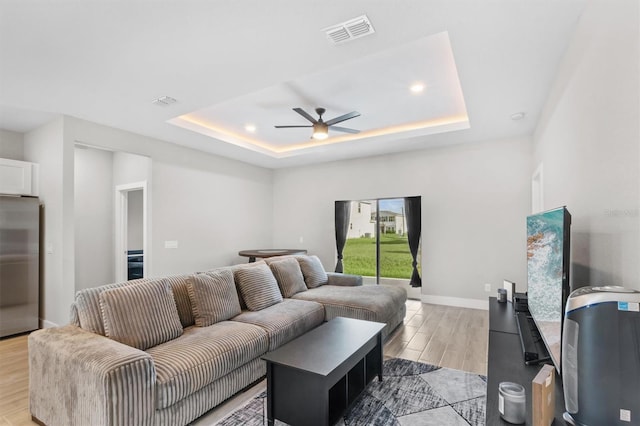 living room featuring ceiling fan, light hardwood / wood-style floors, and a tray ceiling