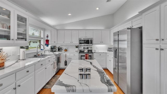 kitchen with stainless steel appliances, white cabinets, sink, vaulted ceiling, and light hardwood / wood-style flooring