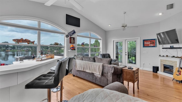 living room with lofted ceiling, a water view, ceiling fan, light hardwood / wood-style floors, and a fireplace