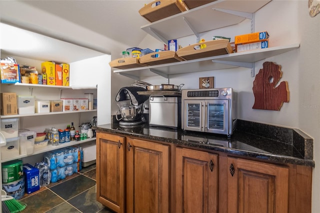 kitchen with open shelves, dark stone counters, brown cabinets, and a toaster
