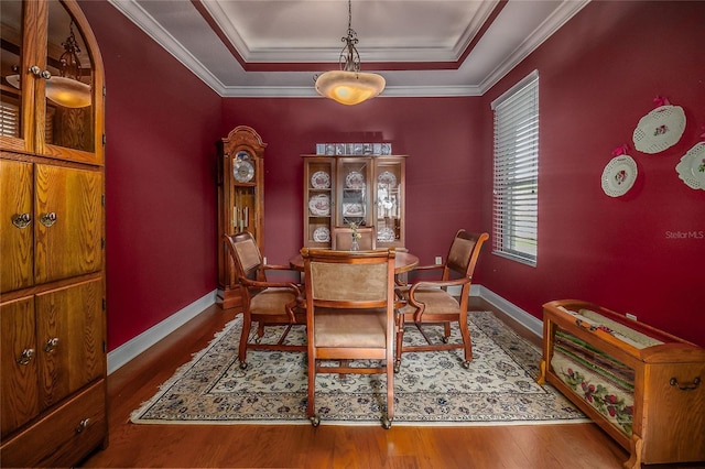 dining space featuring baseboards, crown molding, a tray ceiling, and wood finished floors