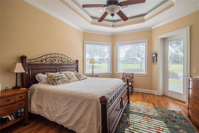 bedroom featuring a tray ceiling, wood finished floors, crown molding, baseboards, and access to exterior