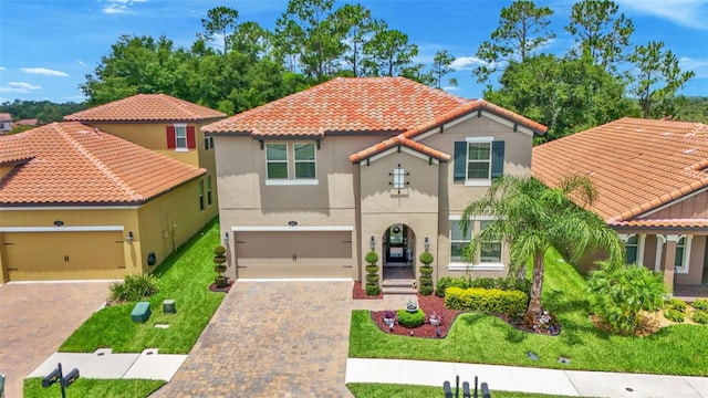 mediterranean / spanish home with a garage, a tiled roof, decorative driveway, a front lawn, and stucco siding