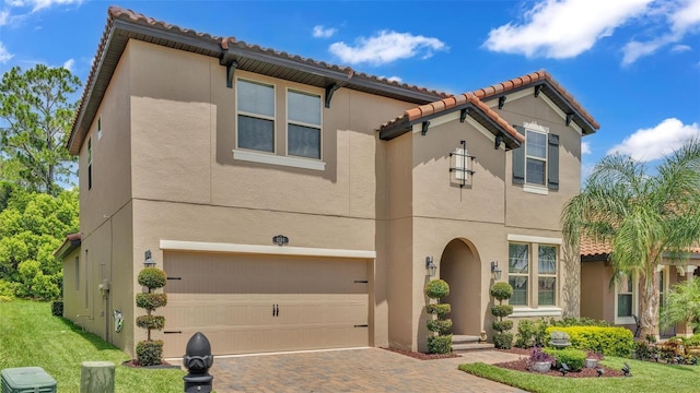 mediterranean / spanish house featuring decorative driveway, an attached garage, a front lawn, and stucco siding