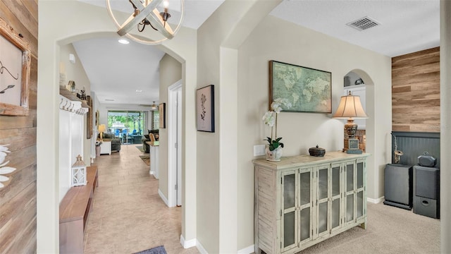 hallway with arched walkways, a chandelier, wood walls, visible vents, and baseboards