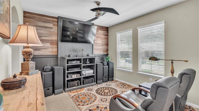 living room with a ceiling fan, wood walls, and baseboards