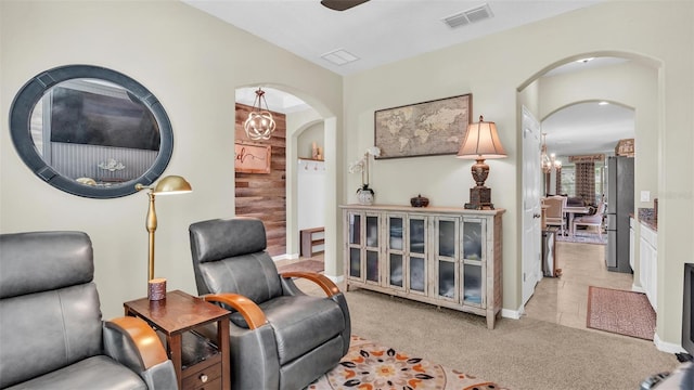 living area with light carpet, visible vents, arched walkways, and ceiling fan with notable chandelier