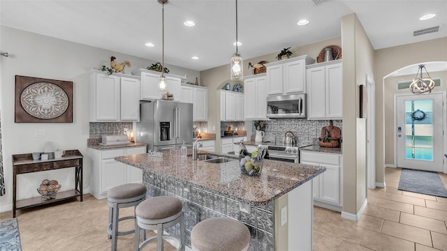 kitchen featuring a breakfast bar, pendant lighting, a center island with sink, stainless steel appliances, and visible vents