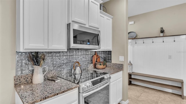 kitchen with appliances with stainless steel finishes, dark stone counters, white cabinets, and backsplash