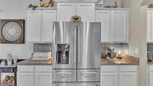 kitchen with dark stone counters, high end fridge, white cabinetry, and backsplash