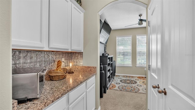 kitchen featuring arched walkways, backsplash, a ceiling fan, white cabinetry, and light stone countertops