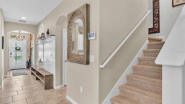 interior space featuring light tile patterned floors, baseboards, visible vents, arched walkways, and stairway