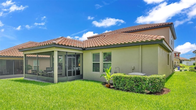 back of property with a yard, a tiled roof, a sunroom, and stucco siding