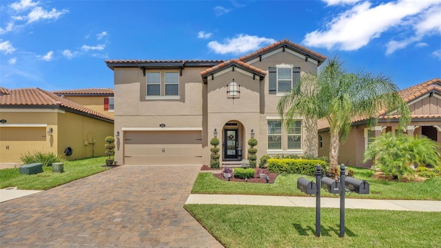 mediterranean / spanish-style house featuring a garage, a front yard, decorative driveway, and stucco siding