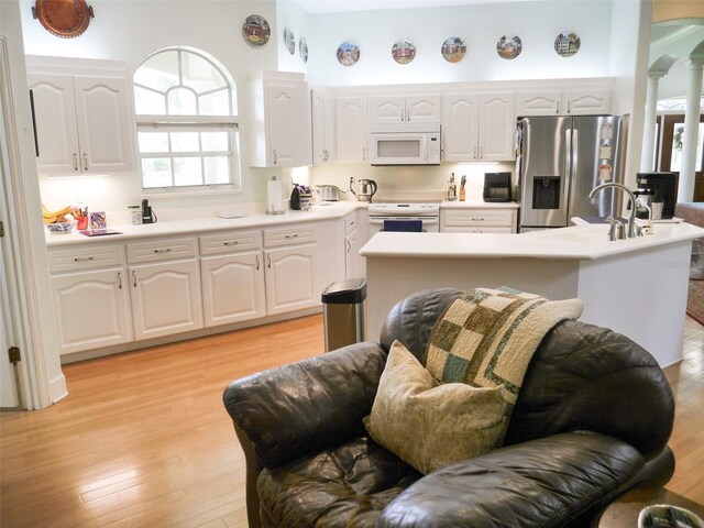 kitchen with white appliances, ornate columns, light hardwood / wood-style floors, sink, and white cabinets