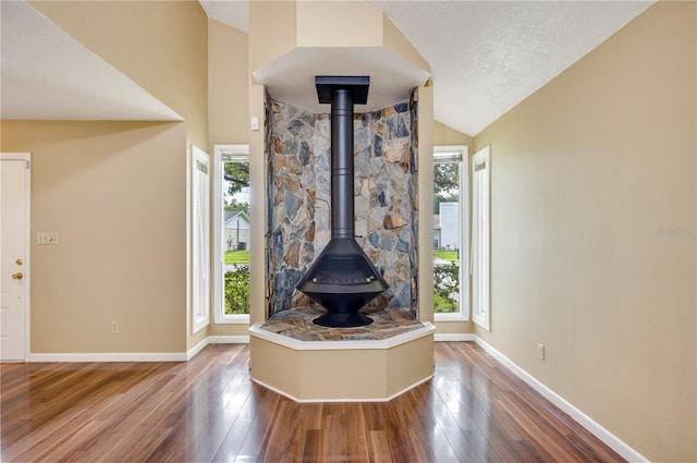 unfurnished living room with hardwood / wood-style flooring, vaulted ceiling, a wood stove, and a wealth of natural light