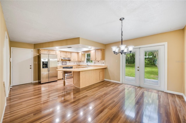 kitchen with light brown cabinetry, a kitchen bar, light hardwood / wood-style floors, kitchen peninsula, and stainless steel appliances