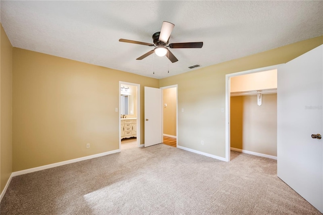 unfurnished bedroom with ensuite bathroom, a walk in closet, light colored carpet, a closet, and ceiling fan