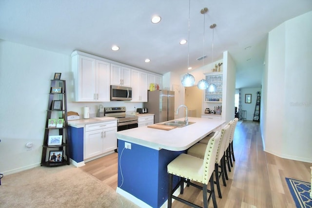 kitchen with sink, appliances with stainless steel finishes, a kitchen island with sink, hanging light fixtures, and white cabinets