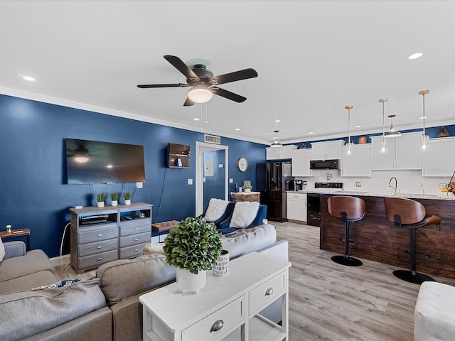 living room featuring ornamental molding, light wood-type flooring, ceiling fan, and sink