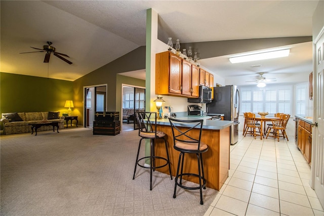 kitchen featuring ceiling fan, kitchen peninsula, vaulted ceiling, a breakfast bar area, and light colored carpet