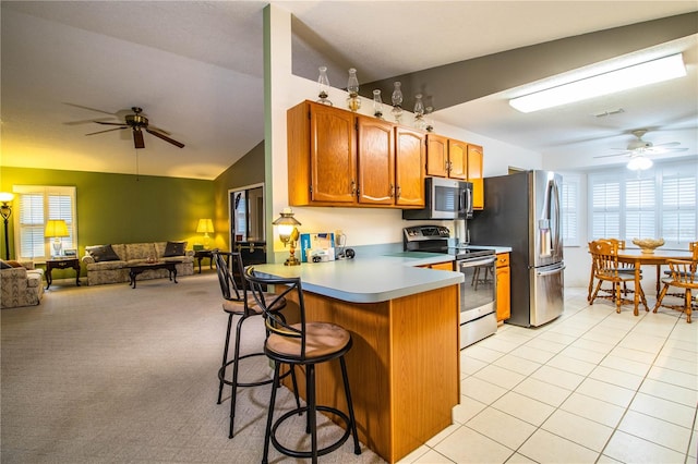 kitchen featuring a kitchen breakfast bar, stainless steel appliances, vaulted ceiling, light colored carpet, and kitchen peninsula