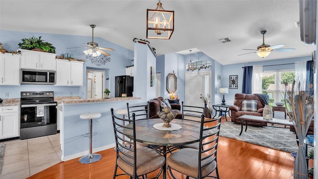 dining area with vaulted ceiling, ceiling fan with notable chandelier, and light hardwood / wood-style floors