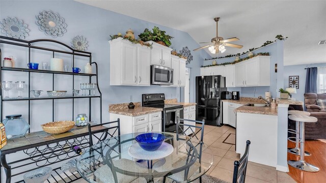 kitchen featuring appliances with stainless steel finishes, white cabinetry, kitchen peninsula, vaulted ceiling, and light tile patterned floors