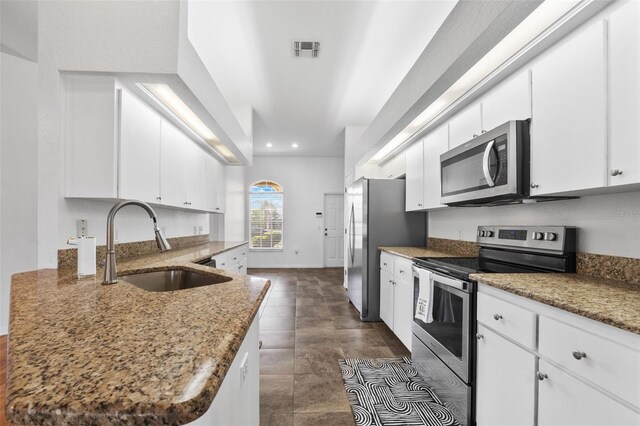 kitchen featuring appliances with stainless steel finishes, sink, dark stone countertops, and white cabinets
