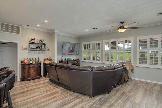 living room featuring indoor bar, crown molding, a textured ceiling, and light wood-type flooring