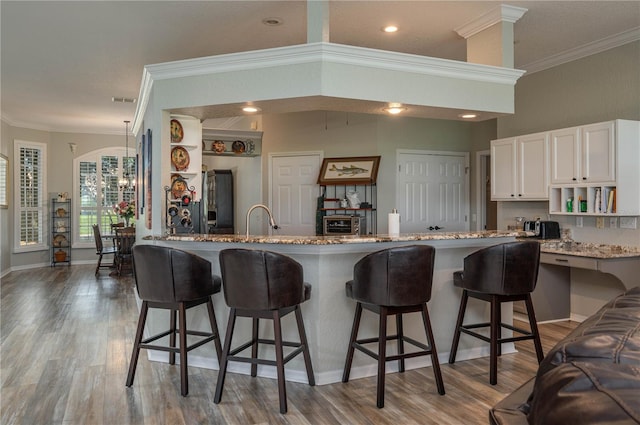 kitchen with a kitchen bar, light stone counters, crown molding, kitchen peninsula, and white cabinets