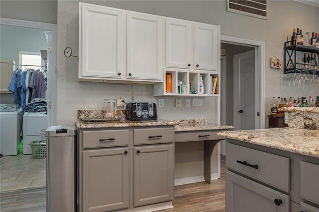 kitchen with white cabinetry, light wood-type flooring, washing machine and clothes dryer, and light stone counters