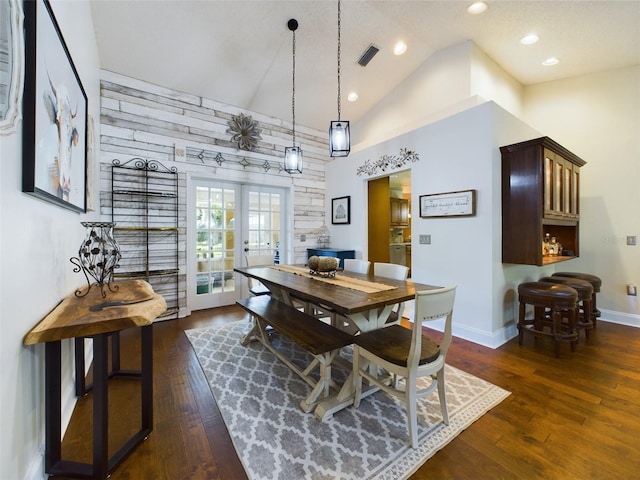 dining area featuring high vaulted ceiling, french doors, dark hardwood / wood-style floors, and wooden walls