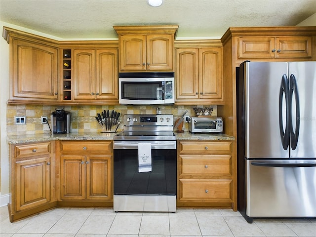 kitchen featuring appliances with stainless steel finishes, decorative backsplash, light tile patterned floors, and light stone countertops