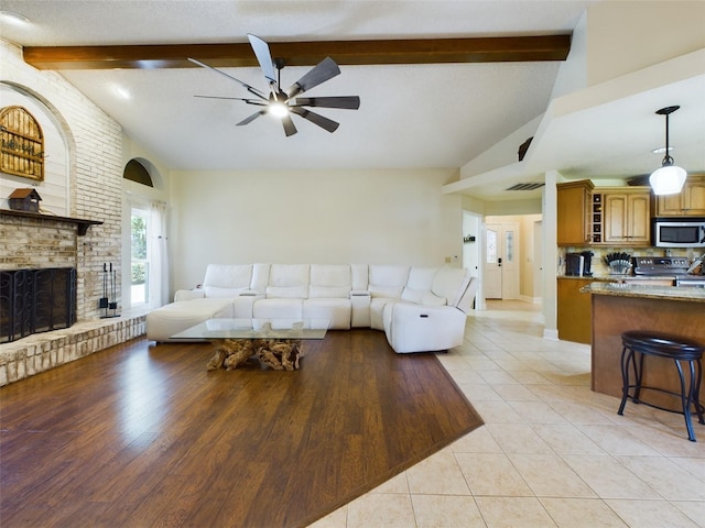 living room featuring light hardwood / wood-style floors, vaulted ceiling with beams, ceiling fan, and a brick fireplace