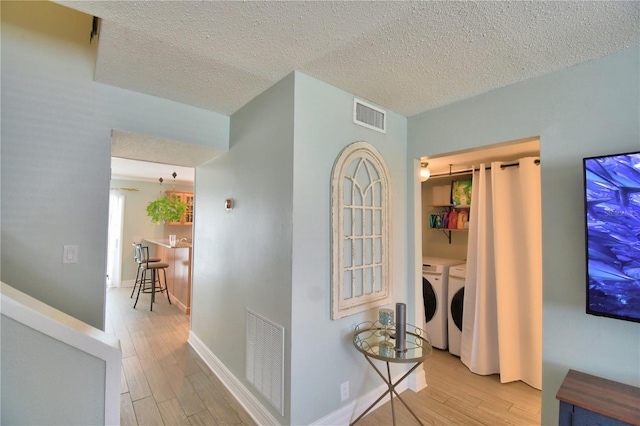 hall with light hardwood / wood-style flooring, washing machine and dryer, and a textured ceiling