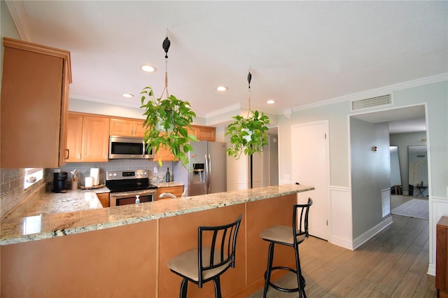 kitchen with a breakfast bar, light hardwood / wood-style flooring, kitchen peninsula, stainless steel appliances, and decorative backsplash