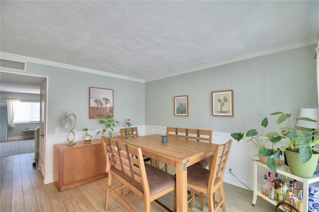 dining room featuring ornamental molding, light hardwood / wood-style floors, and a textured ceiling