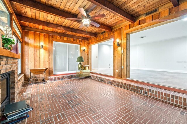 unfurnished sunroom with beamed ceiling, ceiling fan, wood ceiling, and a brick fireplace