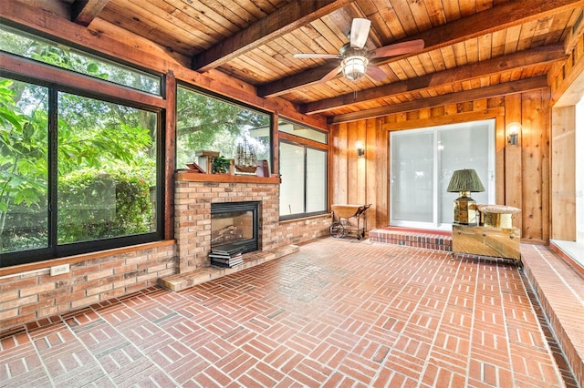 unfurnished sunroom featuring beamed ceiling, wooden ceiling, ceiling fan, and a fireplace