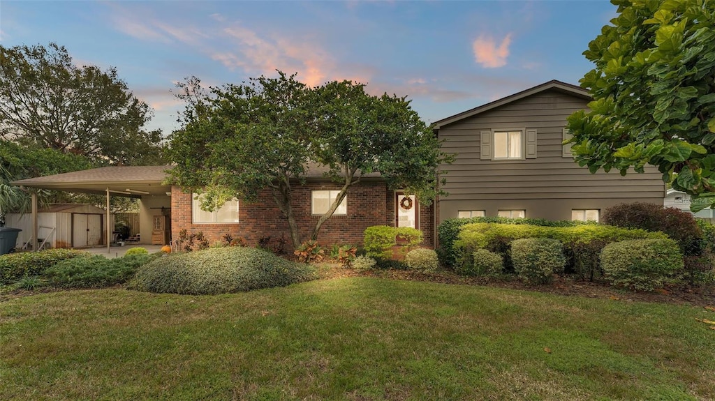 tri-level home with a carport, a storage shed, and a lawn